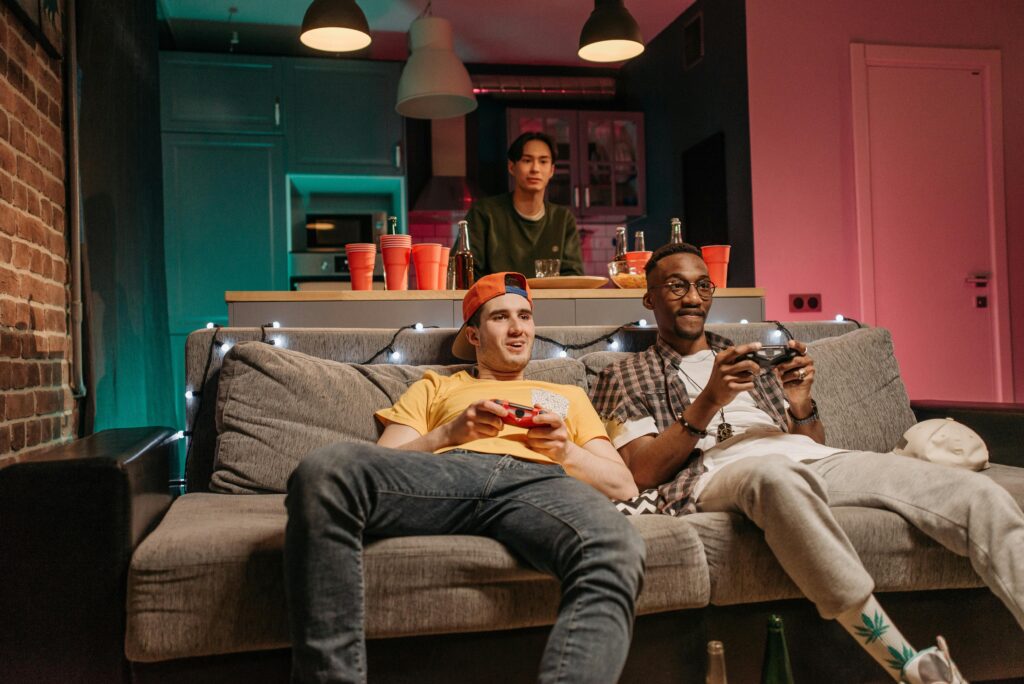 Three friends having a relaxed evening playing video games at home with drinks.