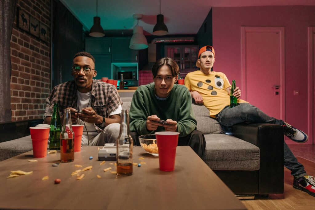 Three young men playing video games and enjoying drinks in a modern living room setting.